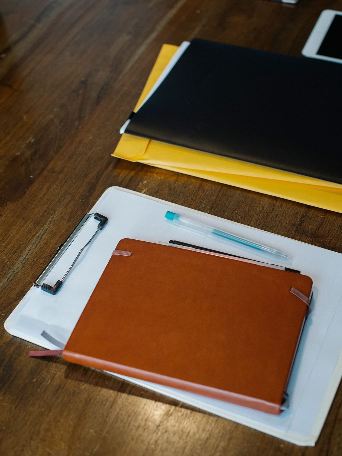 A clipboard, a notebook and a pen on a desk