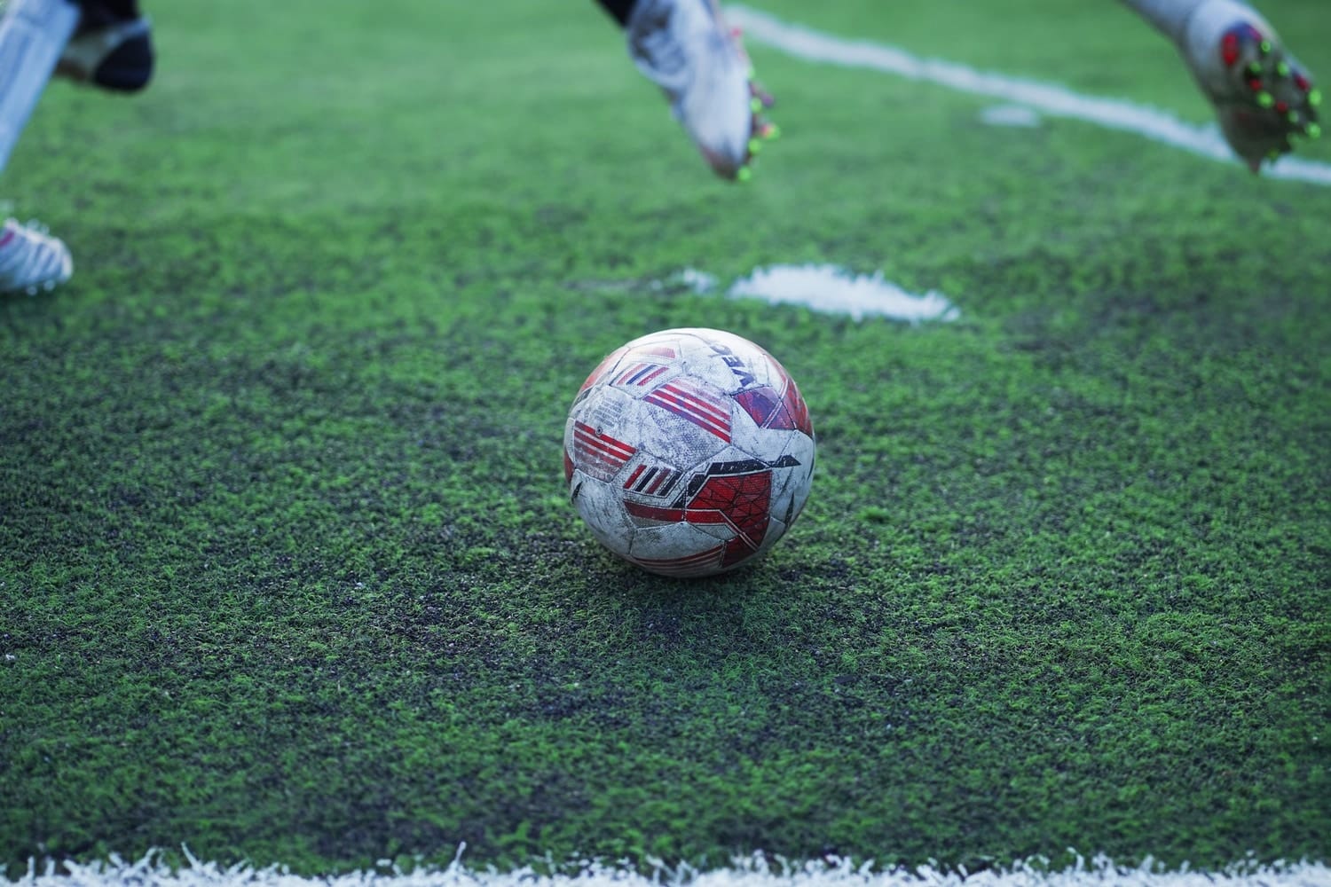 A football on wet grass with players' boots in motion